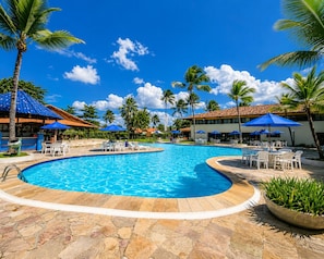A swimming pool with lounge chairs and umbrellas, surrounded by palm trees and a clear sky.