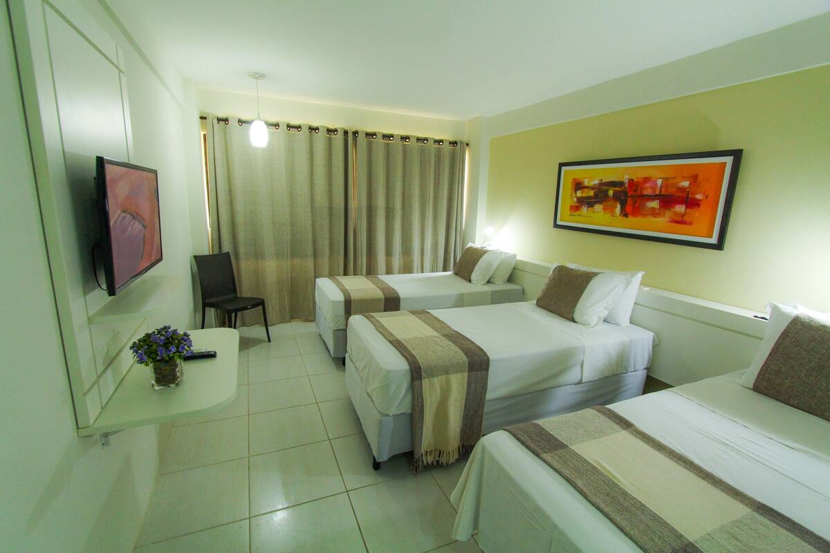 Habitación de hotel con dos camas, televisión, una silla y un cuadro en la pared.