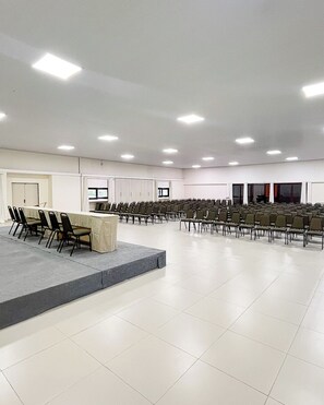 A large conference room with rows of chairs, a long table, and a stage area.