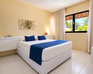 Habitación de hotel impecable con una cama, un cuadro en la pared, una ventana con cortinas y vistas a palmeras.