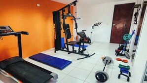 Un gimnasio con cinta de correr, banco de pesas, estructura para sentadillas y varios pesas.
