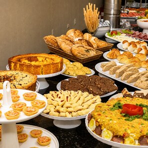 A buffet with various baked goods, including bread, pastries, and a cake. - Orange Praia Hotel (Ilha de Itamaraca)