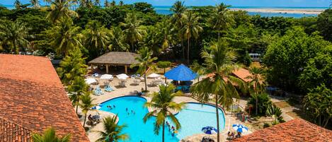 A resort with a central swimming pool surrounded by palm trees and lounge chairs.