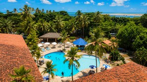 Un resort con piscina central rodeada de palmeras y sillones de descanso.