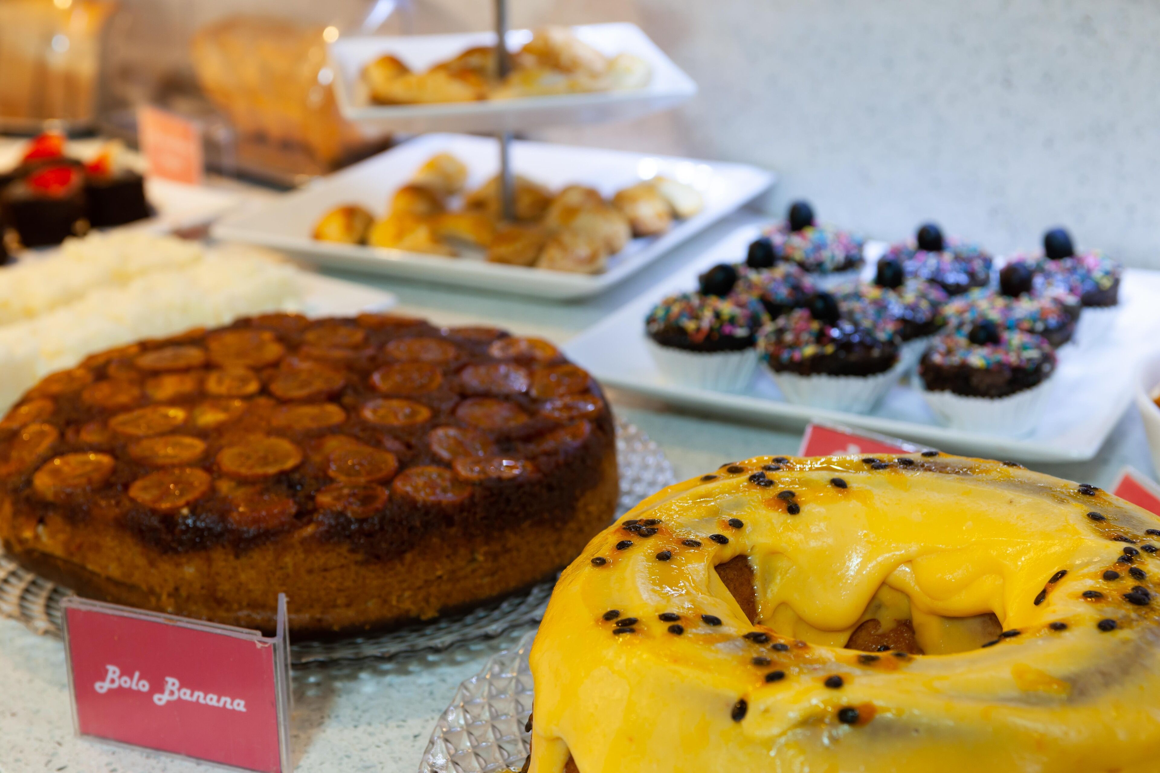 Eine Auswahl an Desserts, darunter ein Bolo Banana Kuchen, ein Karamellkuchen und Cupcakes mit bunten Streuseln.