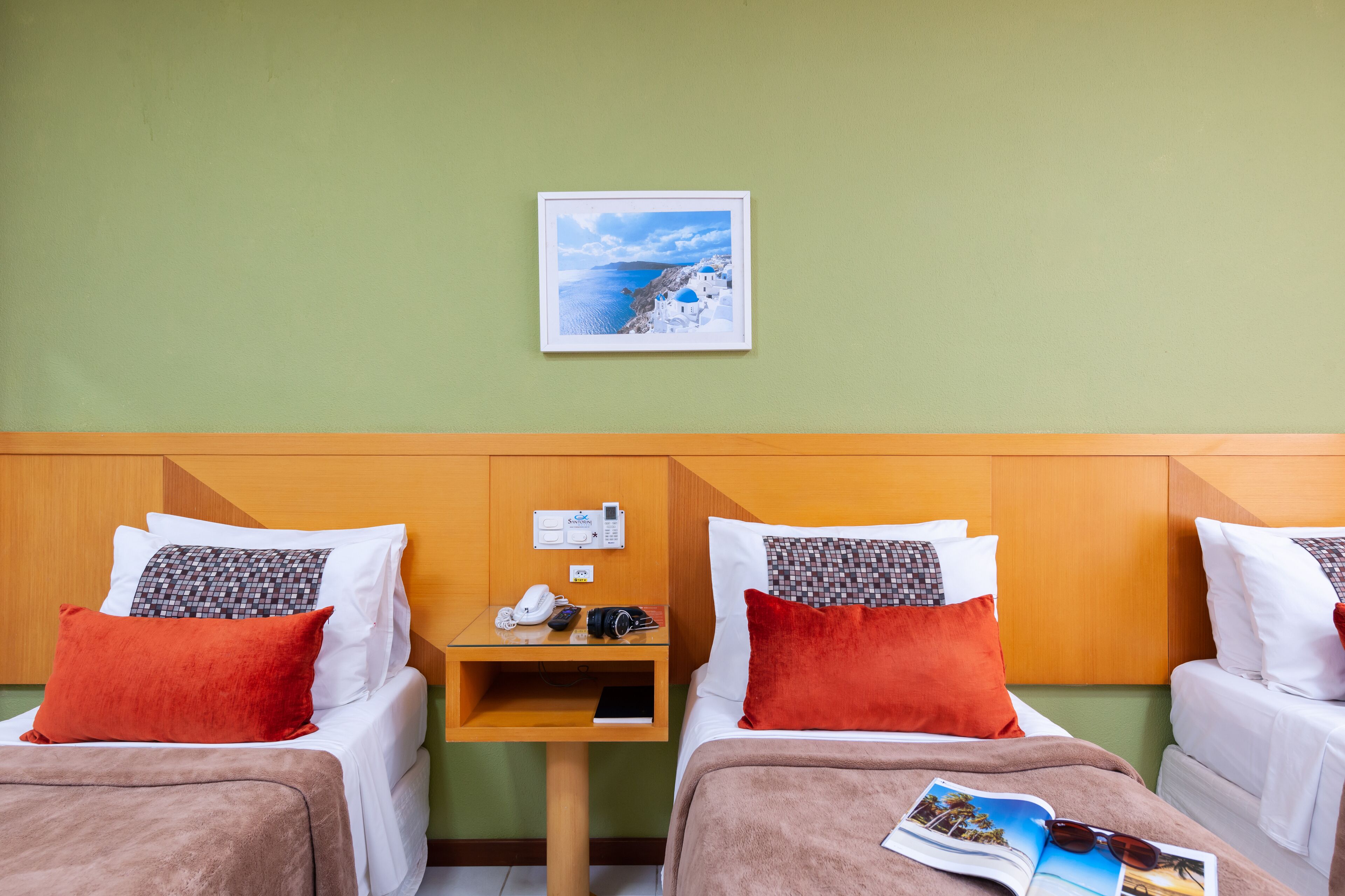 Ein Hotelzimmer mit zwei Betten, einem kleinen Nachttisch, einem gerahmten Bild an der Wand und einer Zeitschrift auf dem Bett.