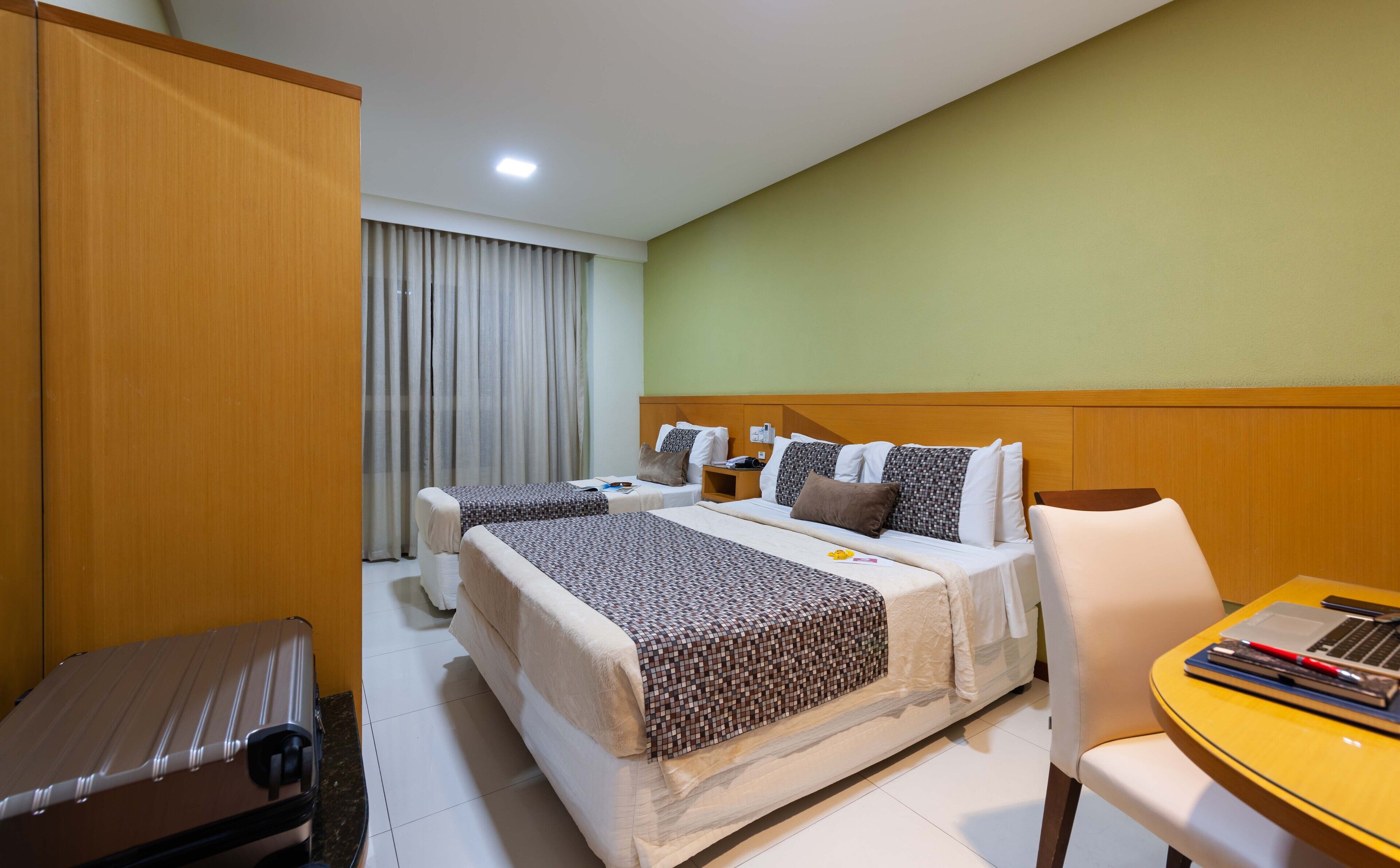 Una habitación de hotel con dos camas, un escritorio, una silla y una maleta.