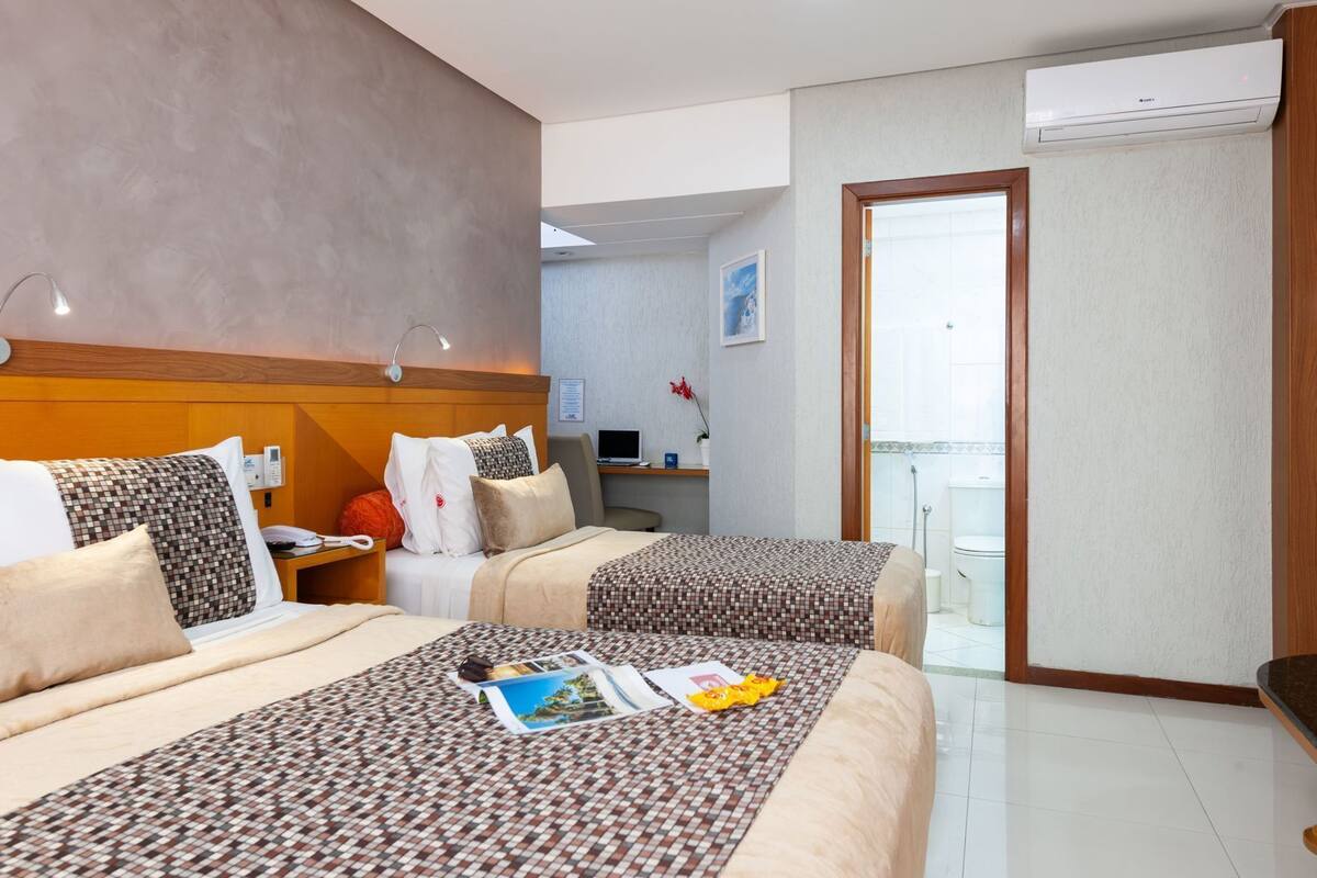 A hotel room with two beds, a desk, a laptop, and a view of the outside.