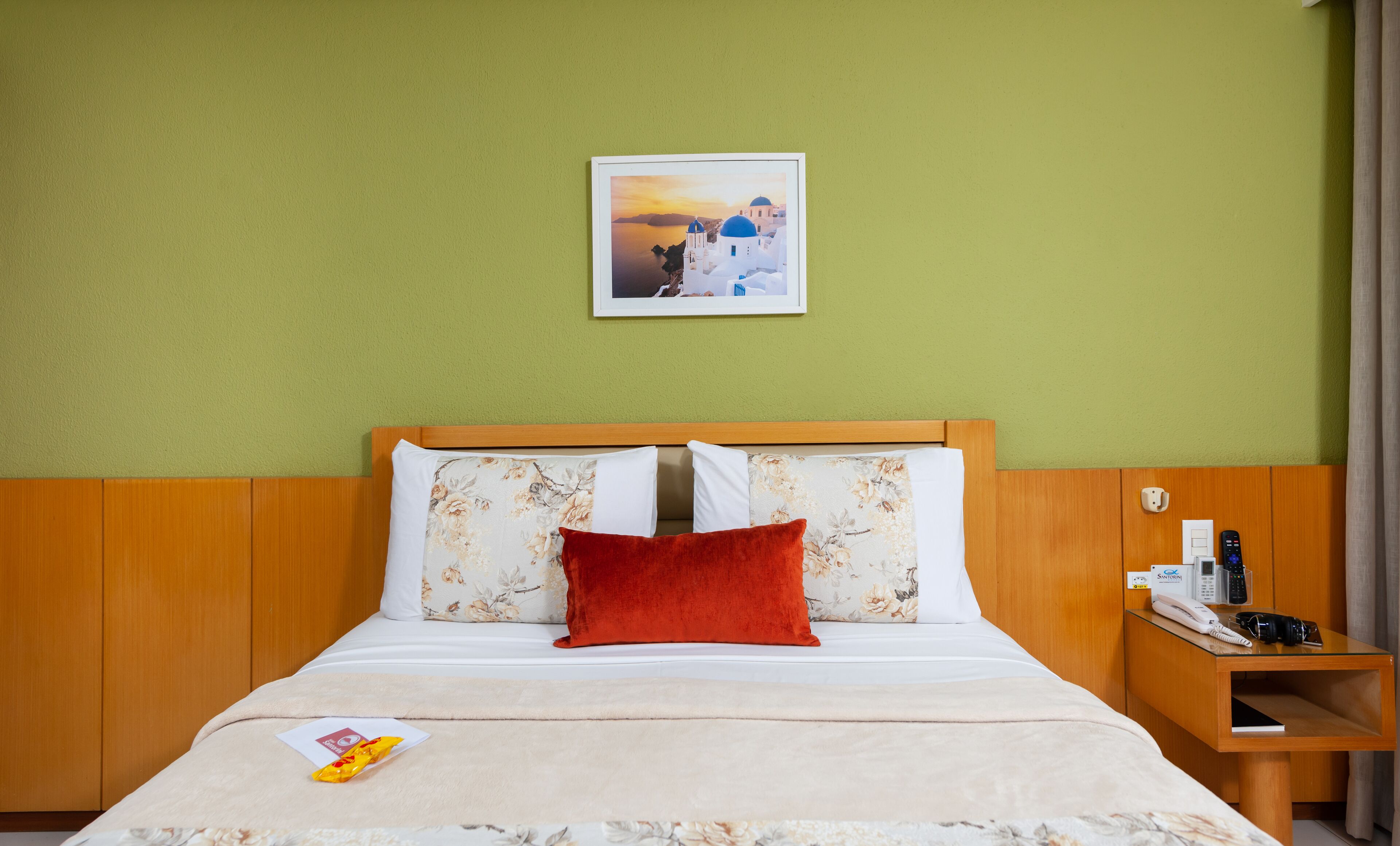 Ein Hotelzimmer mit Bett, Nachttisch, einem gerahmten Bild an der Wand und einem Fenster mit Vorhängen.