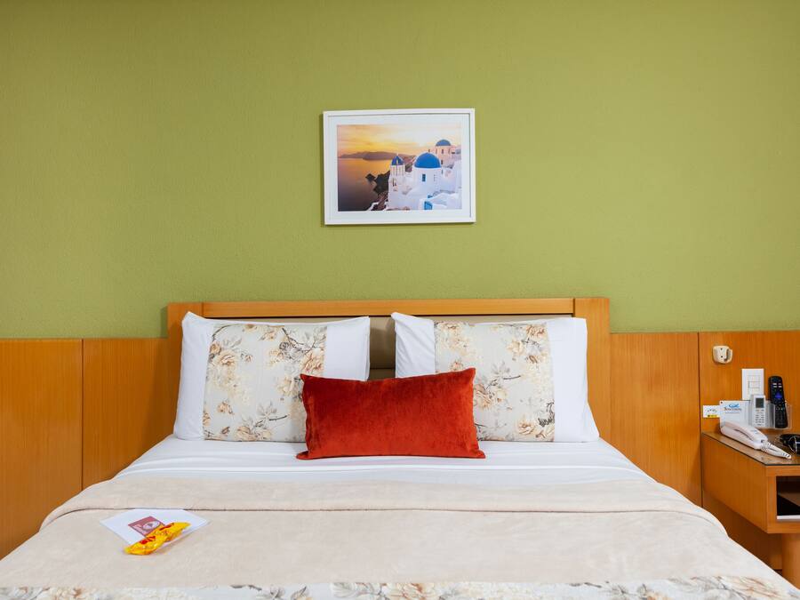 A hotel room with a bed, a nightstand, a framed picture on the wall, and a window with curtains.