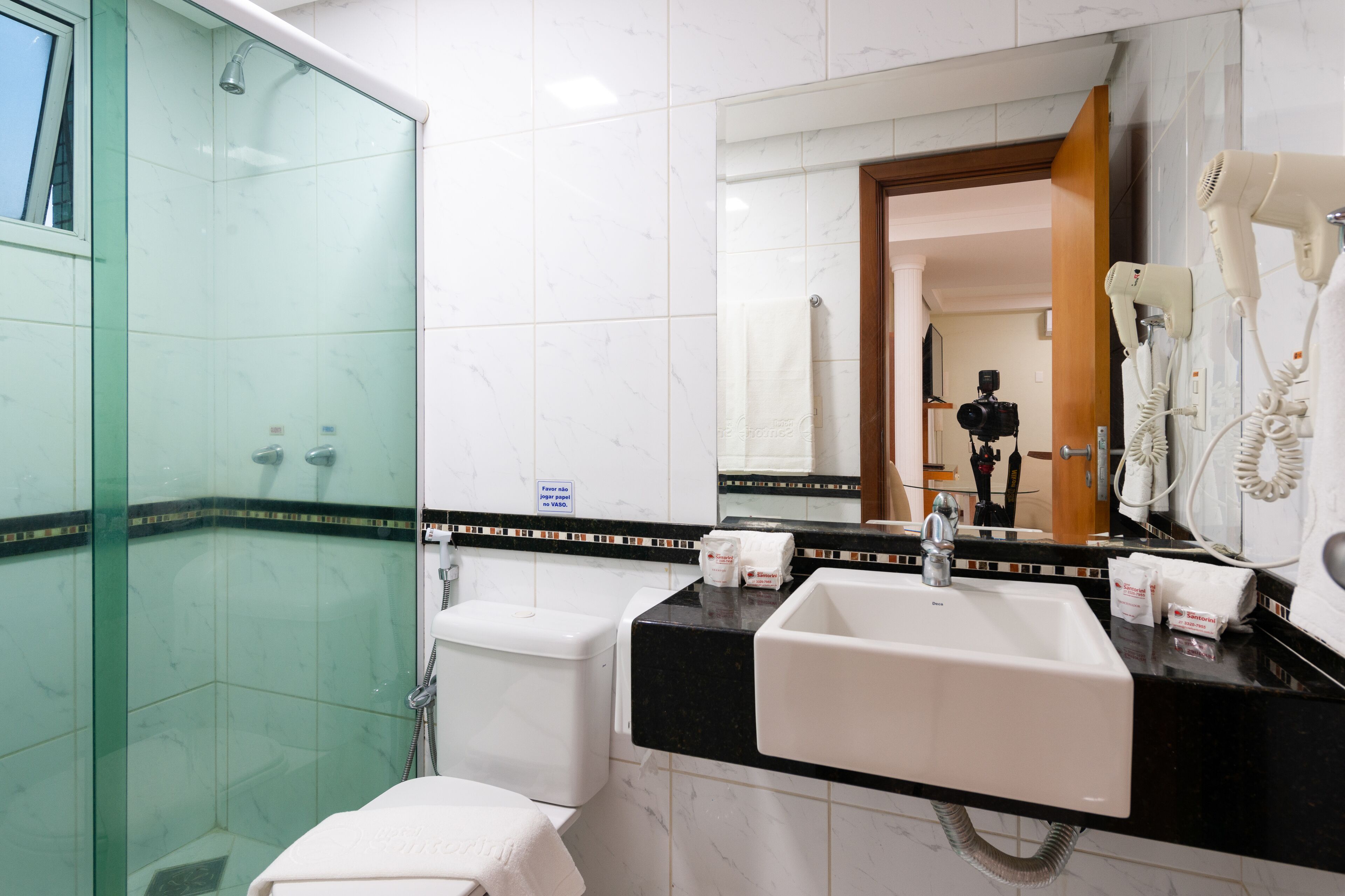 A modern bathroom with a glass-enclosed shower, a white sink with a black countertop, and a mirror reflecting a person in the background.