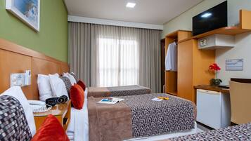 A hotel room with two beds, a desk with a telephone, a television on a stand, and a small refrigerator.