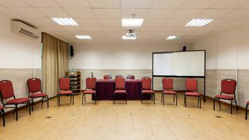 A conference room with a long table, red chairs, a projector screen, and a whiteboard.