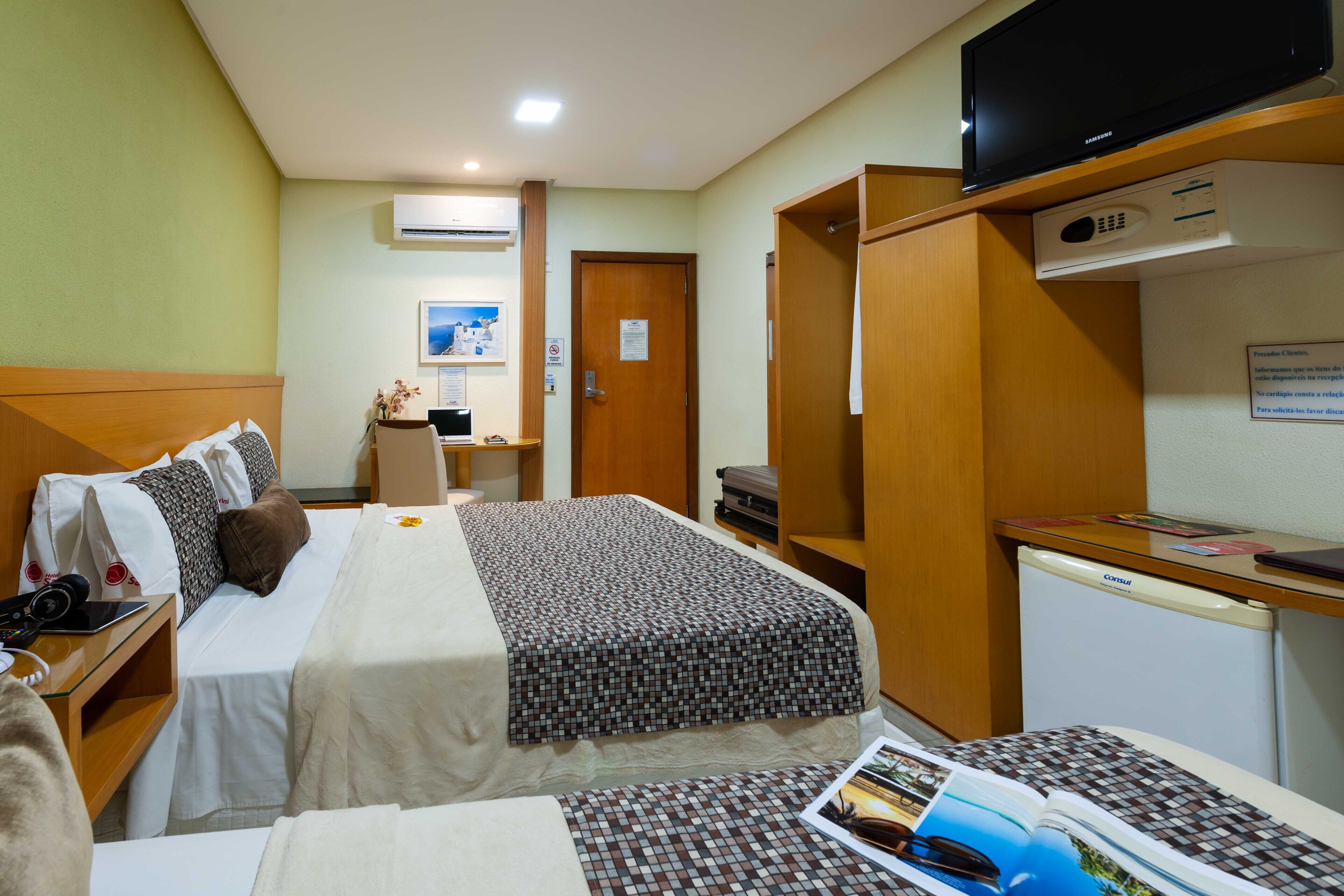 A hotel room with two beds, a desk, a television, and a refrigerator.