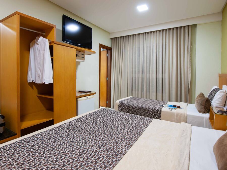 A hotel room with two beds, a TV, a wardrobe, and a desk with a computer.