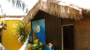 A rustic wooden house with a thatched roof, a hammock, and potted plants. - Chalé Oásis (Galinhos)