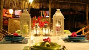 A dining table set with green plates, silverware, and decorative lanterns. - Chalé Oásis (Galinhos)