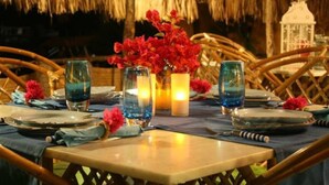 A dining table set with plates, glasses, and a vase of red flowers. - Chalé Oásis (Galinhos)