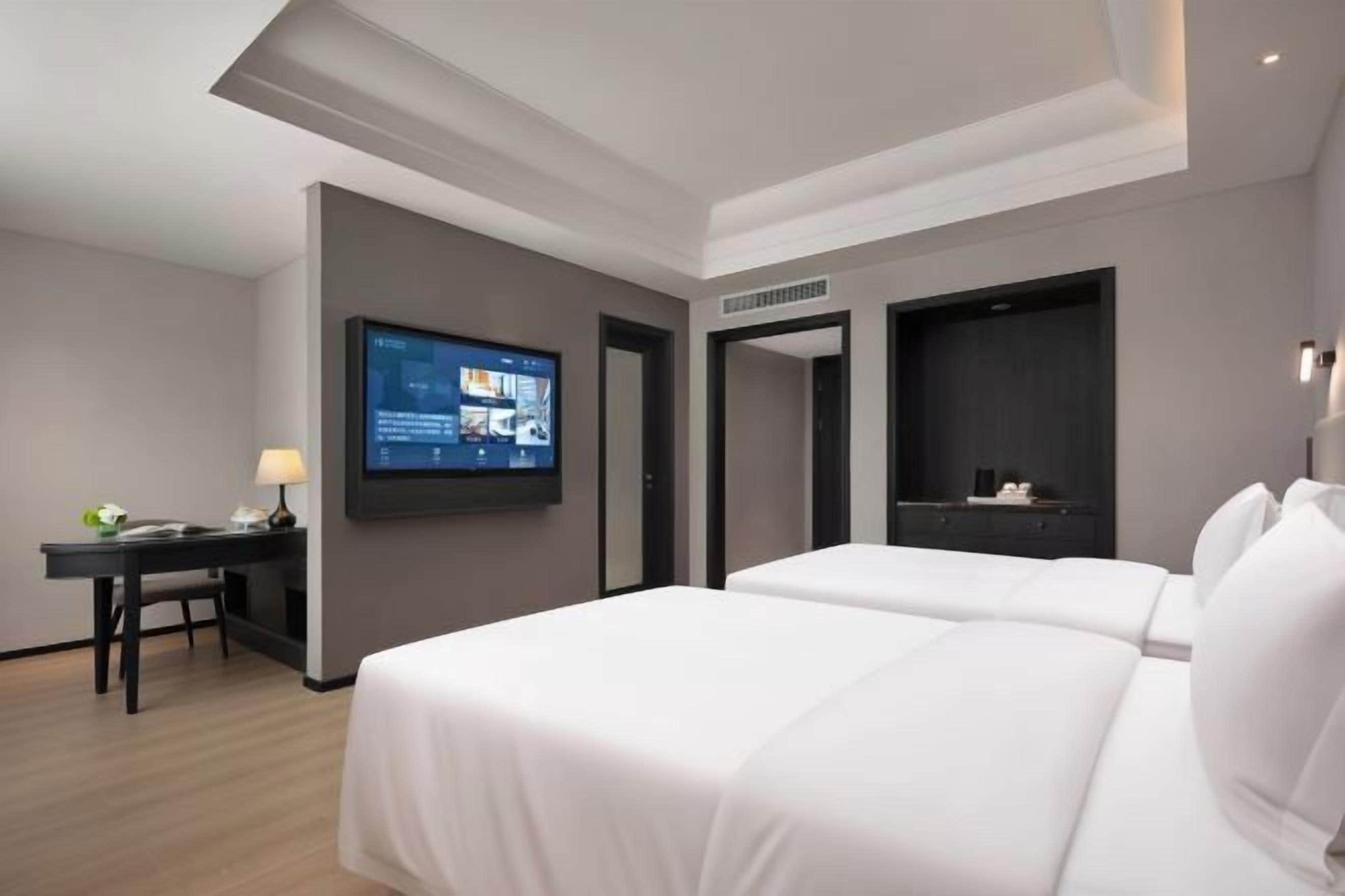 Habitación de hotel con dos camas, un escritorio con lámpara, un televisor de pantalla plana y un mueble de pared oscuro.