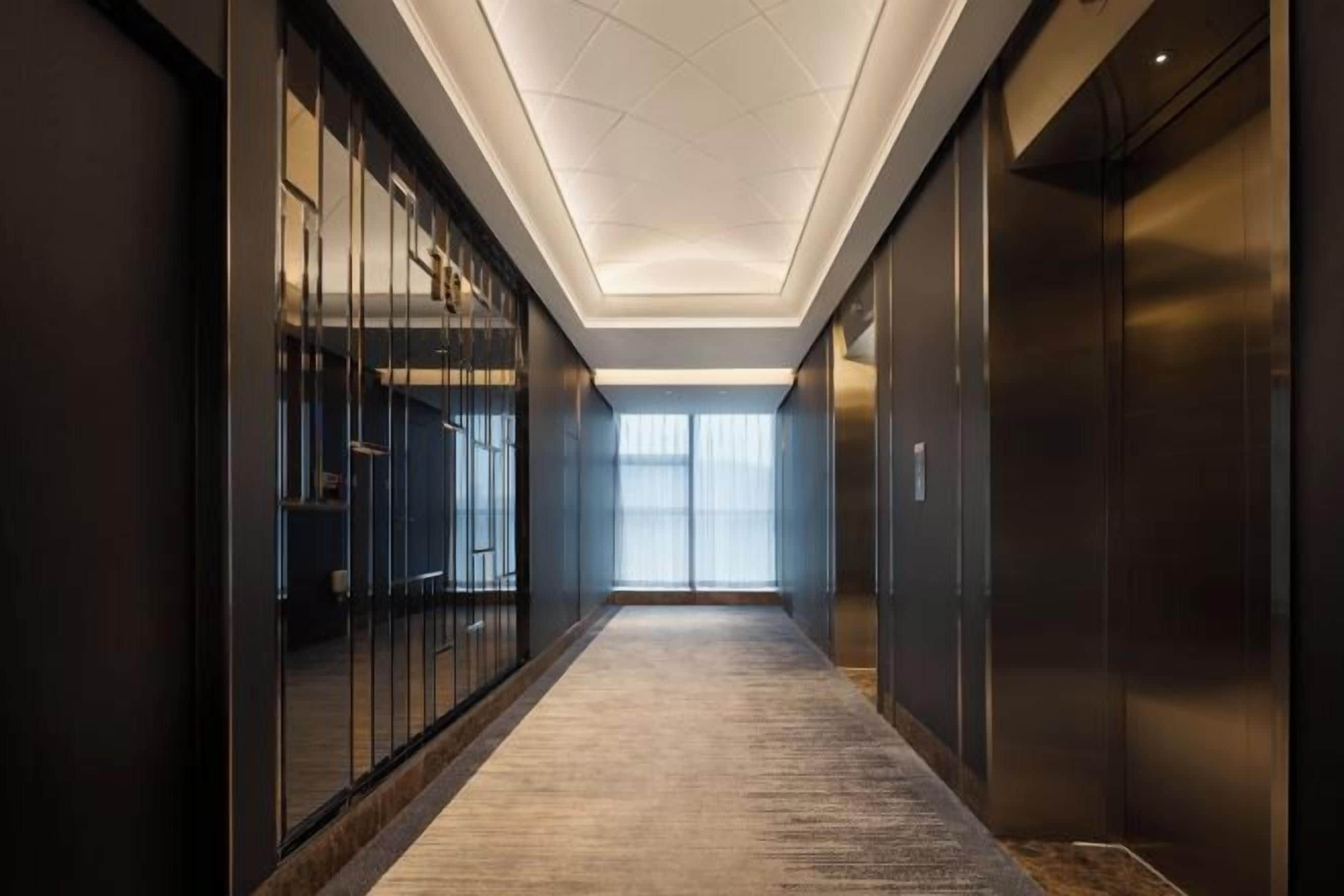 Un pasillo con piso alfombrado, puertas de vidrio e iluminación empotrada en el techo.
