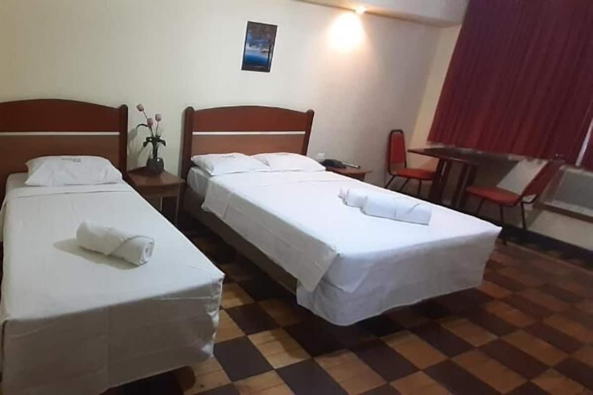 Habitación de hotel con dos camas individuales, una mesita, una silla y una ventana con cortinas.