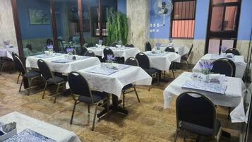 A dining area with multiple tables covered with white tablecloths, arranged in rows.