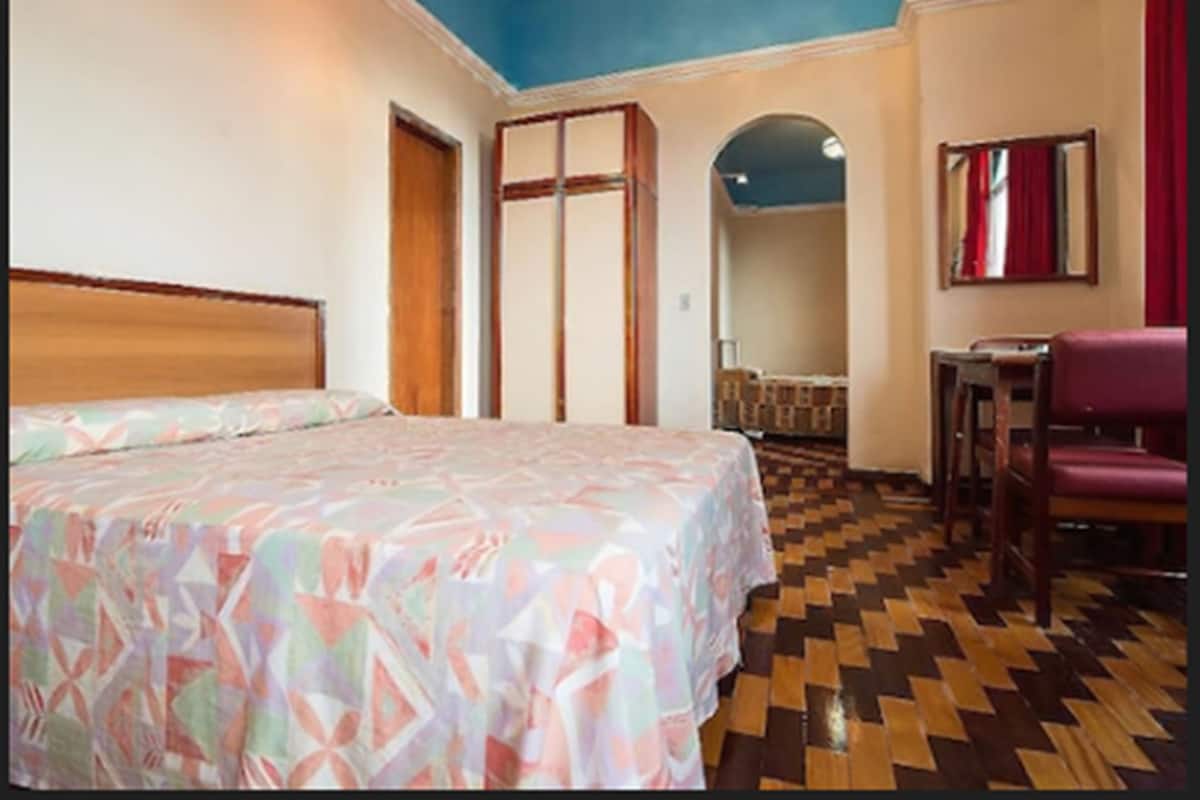 Una habitación de hotel con cama, una silla, una mesita y un espejo.