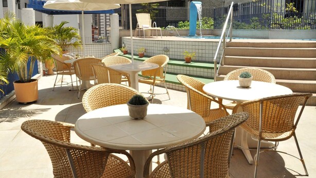 Un patio exterior con mesas y sillas de mimbre, una piscina pequeña y plantas en macetas.