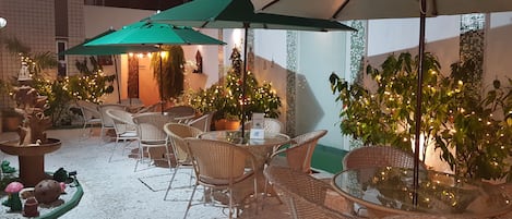 Un patio al aire libre con mobiliario de mimbre, sombrillas verdes y plantas en macetas.