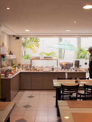 Ein Frühstücksbereich mit Buffet, Tischen, Stühlen und Blick ins Grüne.