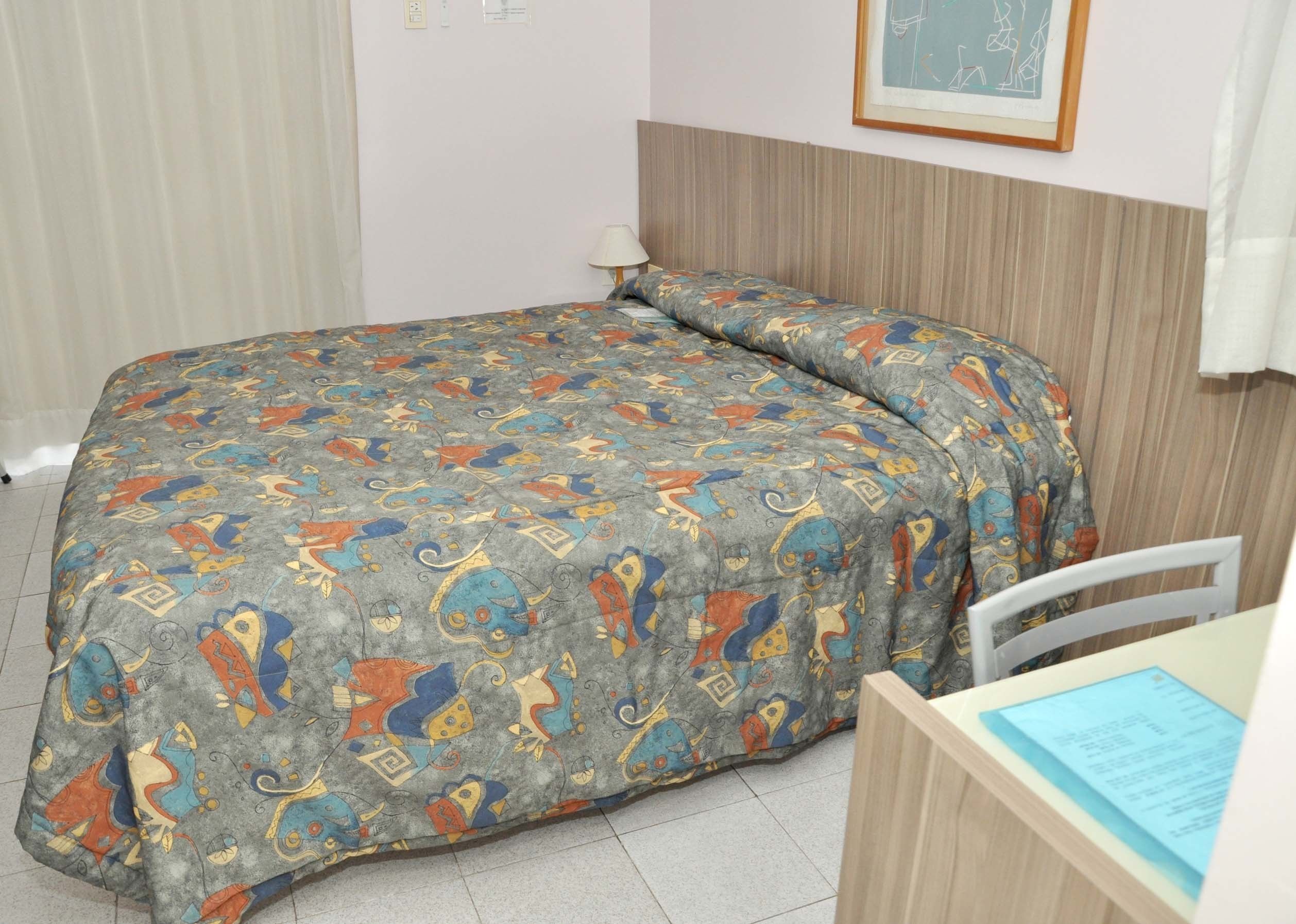 A neatly made bed with a colorful patterned bedspread, a bedside table with a lamp, and a framed picture on the wall.
