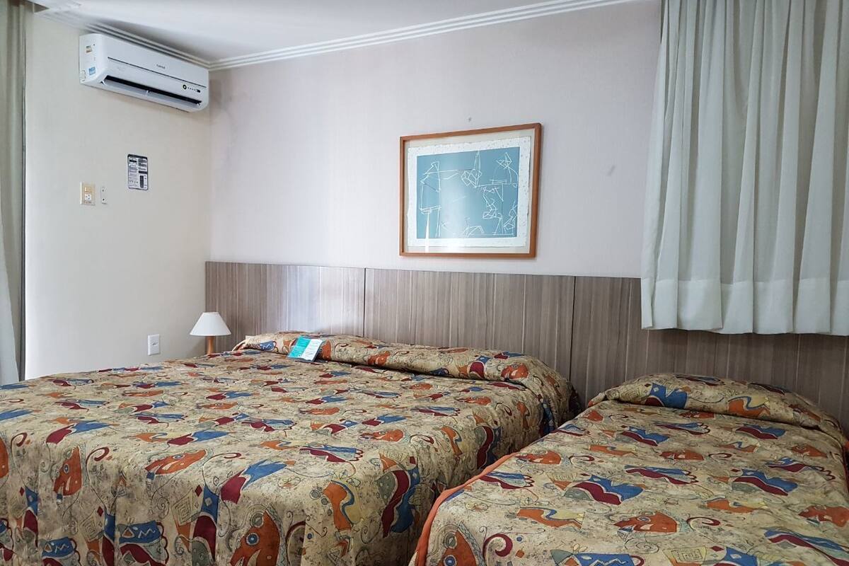 Hotellihuone, jossa on kaksi sänkyä, ilmastointilaite, kehystetty abstrakti taulu ja ikkuna, jossa on verhot.