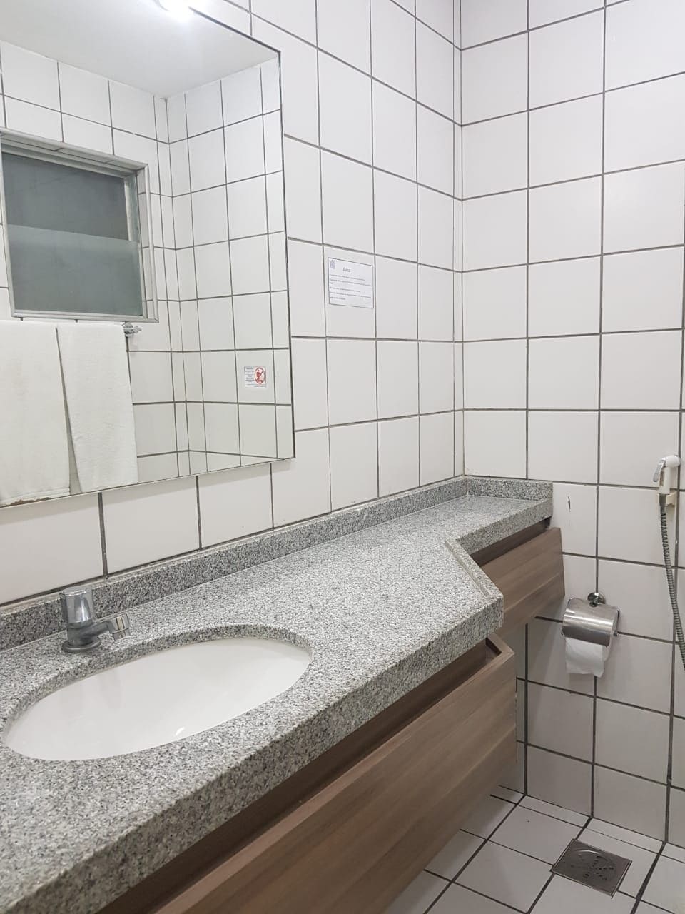 Un baño con lavamanos de encimera de granito, un espejo y pared con azulejos.
