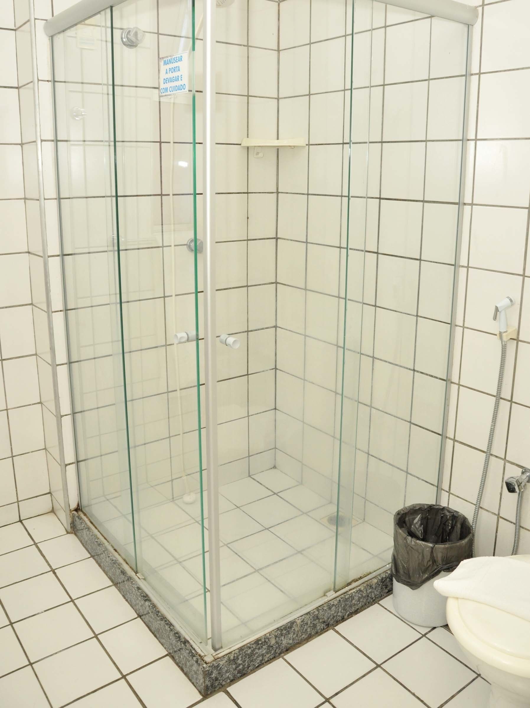 A glass-enclosed shower stall with a tiled floor and a sign advising caution.
