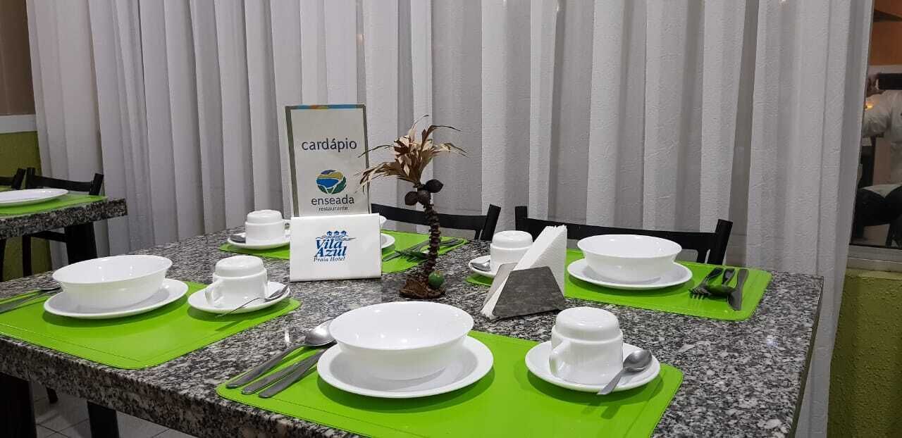 Un comedor de hotel con mesas preparadas para el desayuno, incluyendo cuencos, tazas y cubiertos.
