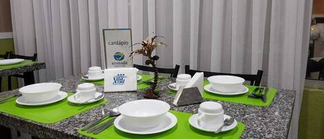 Un comedor de hotel con mesas preparadas para el desayuno, incluyendo cuencos, tazas y cubiertos.