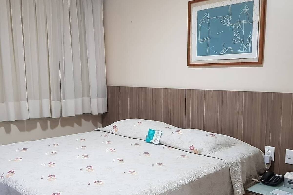 Hotellihuone, jossa on sänky, yöpöytä, puhelin ja seinällä oleva kehystetty abstrakti taulu.