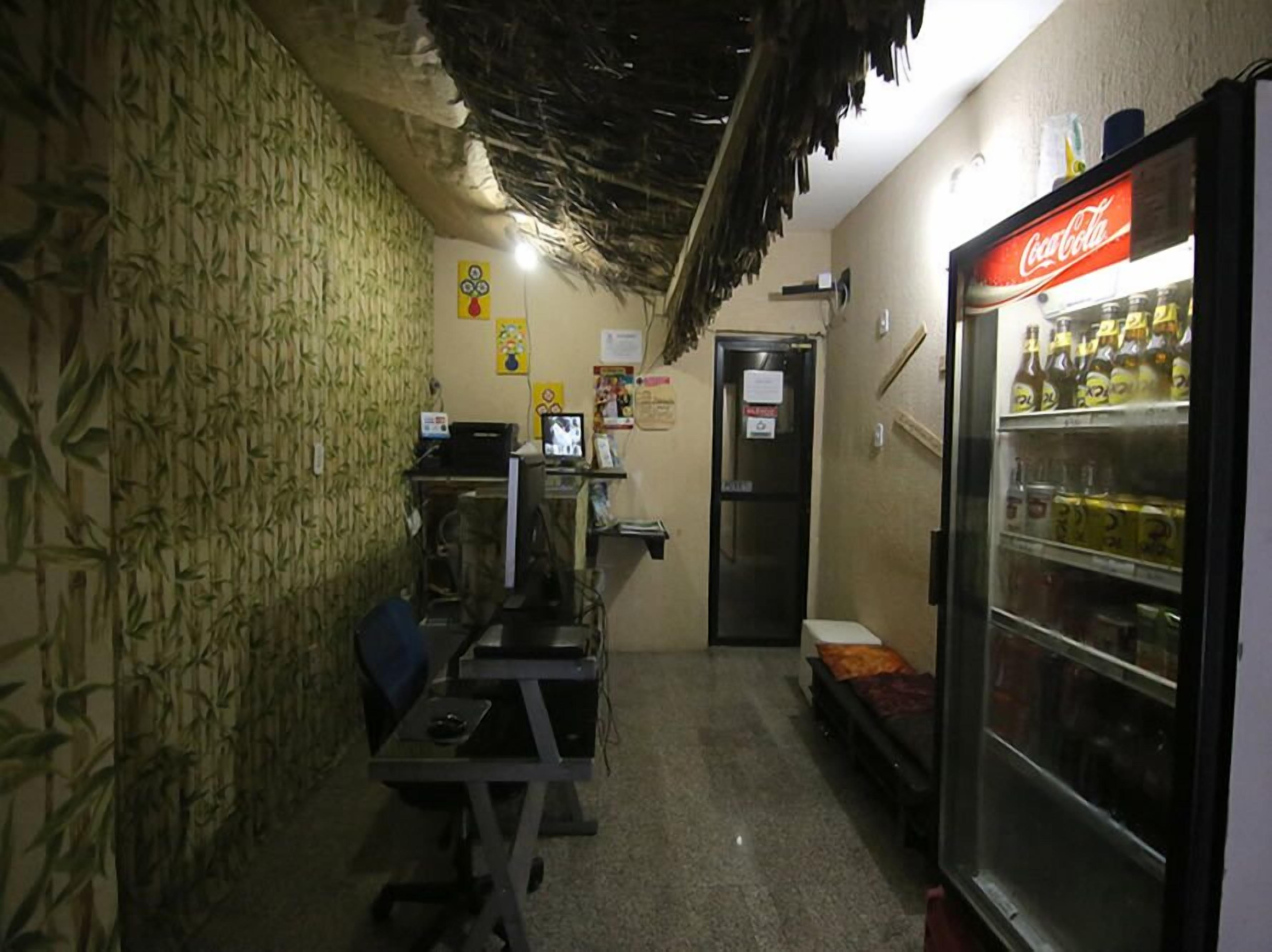 A narrow hallway with a vending machine, a computer, and a small seating area.