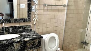 A bathroom with a marble countertop, a white toilet, a glass shower enclosure, and a mirror above the sink.
