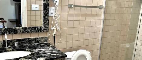 Un baño con encimera de mármol, inodoro blanco, cabina de ducha de cristal y espejo sobre el lavabo.