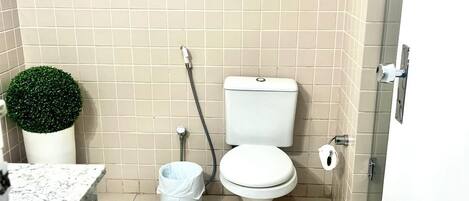Un baño pequeño con inodoro, ducha, lavamanos y una planta en maceta.