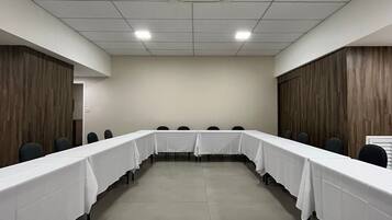 Un salón de conferencias con una larga mesa, sillas y una unidad de aire acondicionado en el techo.