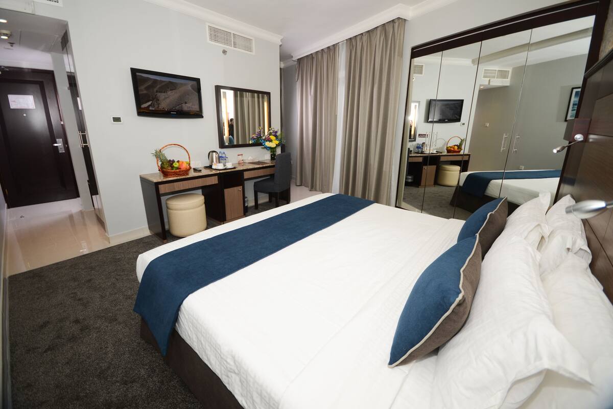 A hotel room with a large bed, a desk with a computer, a mirror, and a television.