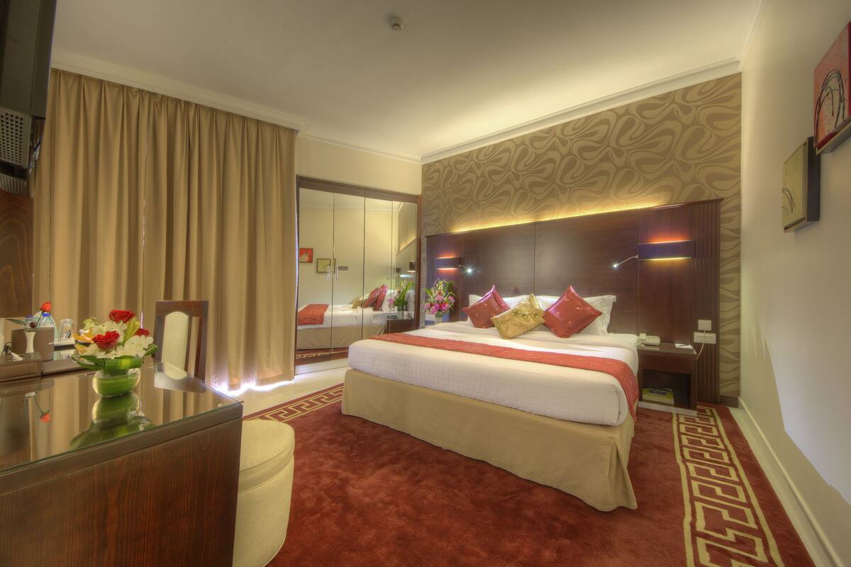 A hotel room with a large bed, a desk, a mirror, and a carpeted floor.