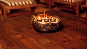 Un tavolo di legno con un posacenere decorativo e candele in una stanza con pareti in pietra e poltrone a righe.