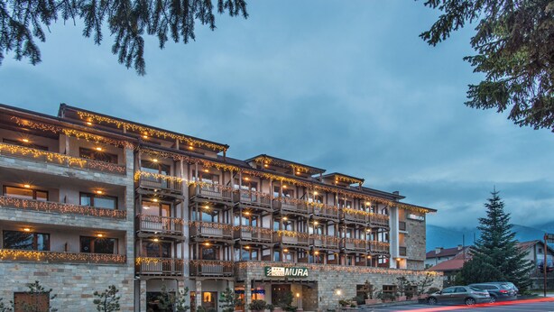 Un hotel a più piani con balconi, un cartello con su scritto 'Hotel Mura' e un parcheggio con auto.
