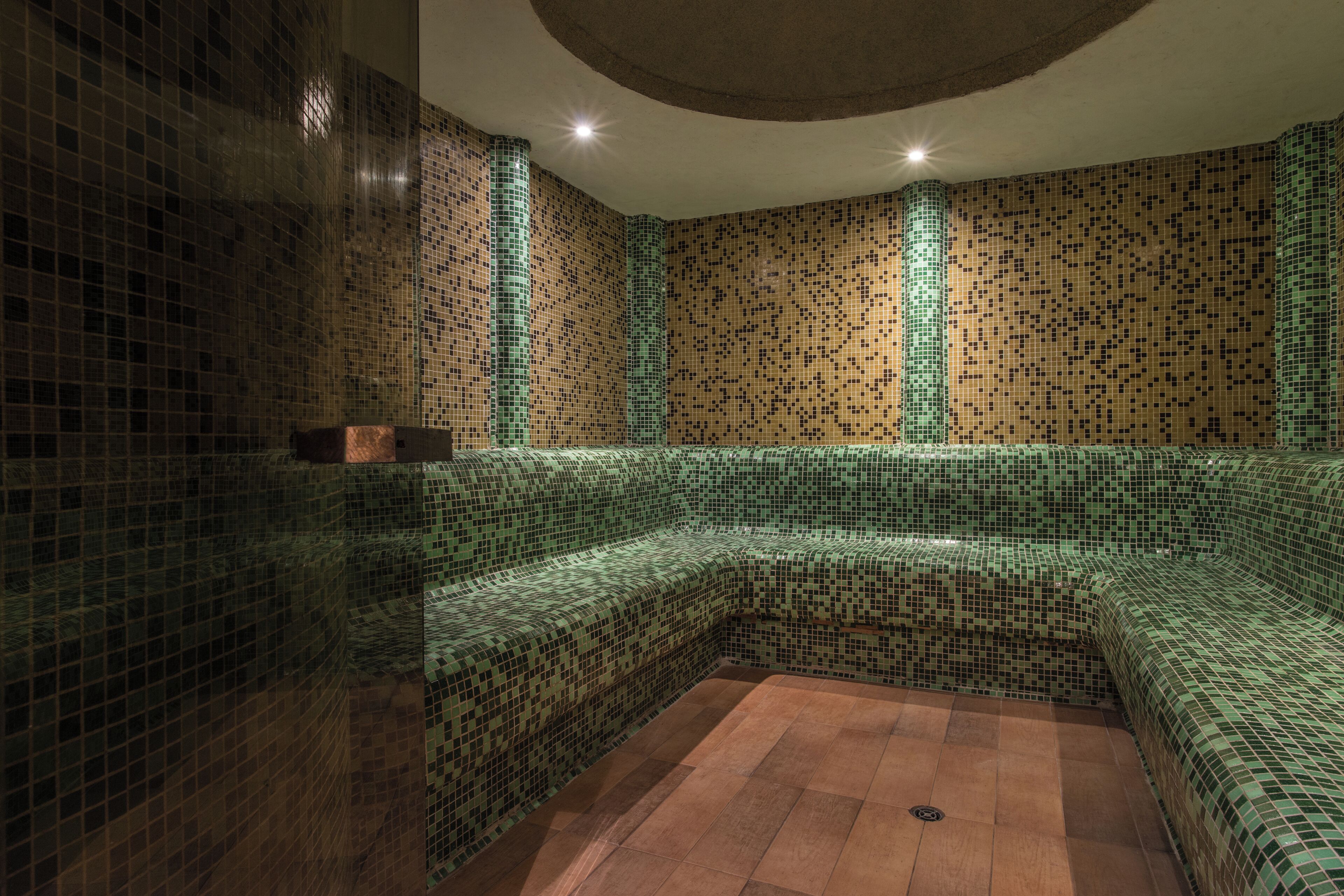 A room with mosaic tile walls, a wooden bench, and a tiled floor.