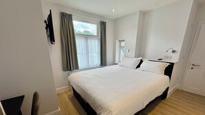 A modern hotel room with a large bed, a desk, and a window with curtains. - Brentwood Hotel (Brentwood)