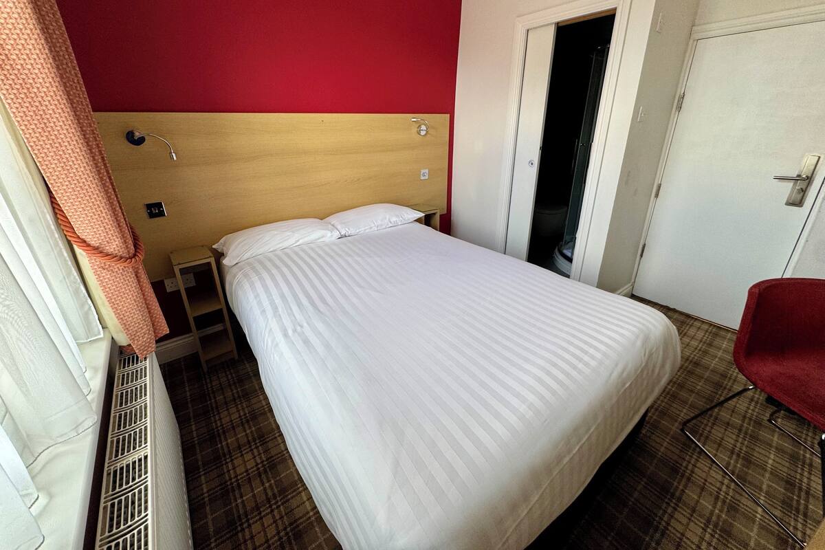 Une chambre d’hôtel avec un lit, un mur rouge, une porte et une chaise rouge.