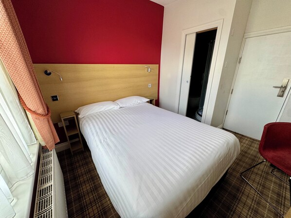 A hotel room with a bed, a red wall, a door, and a red chair. - Brentwood Hotel (Brentwood)